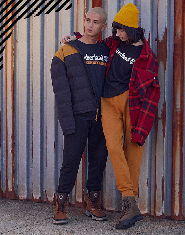 Man and woman in Timberland shirts and boots leaning against wall