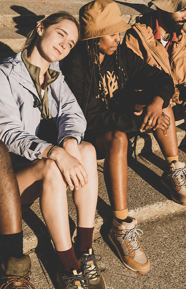 Image of two women sitting side by side on concrete, wearing shorts and Timberland hiking boots.