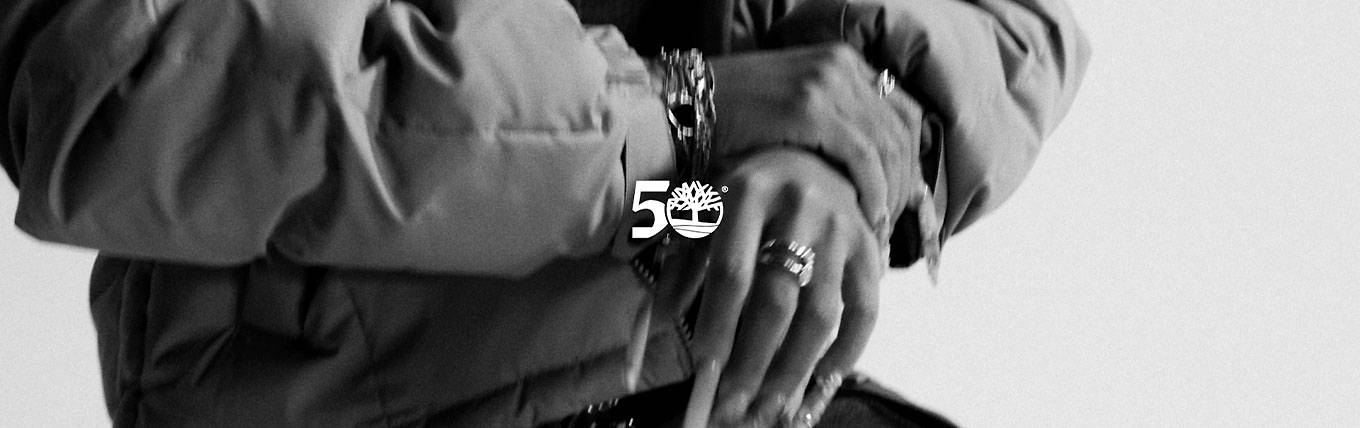 Black-and-white image of a closeup of a woman's torso, wearing a puffy jacket and enormous statement rings/bracelet.