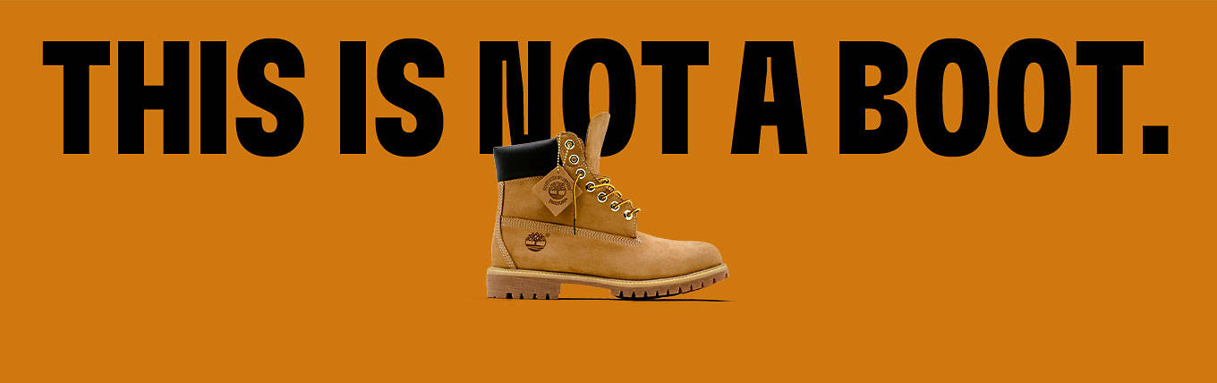 Large black text reading 'This Is Not A Boot' against an orange background. In the foreground is a Timberland 6-inch premium boot in wheat color.