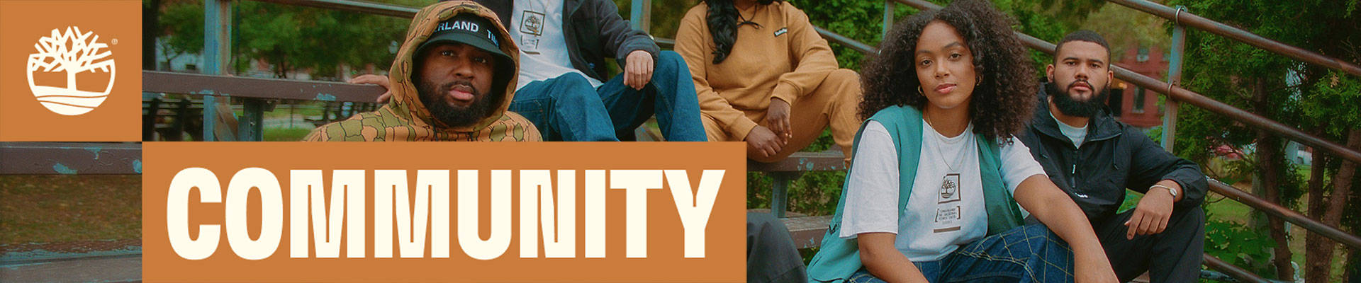 Image of five young friends, two women and three men, all different races, wearing Timberland clothing and footwear, sitting together on blue-and-rust colored bleachers outside against a backdrop of trees.