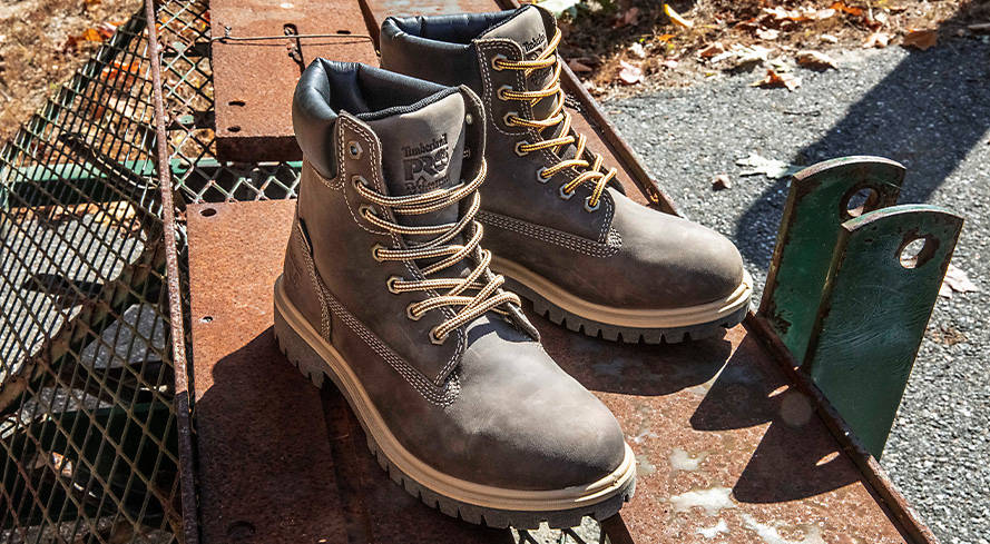 Close-up image of a pair of brown Timberland work boots with tan laces and midsoles, outside on a sunny day atop deck boards.