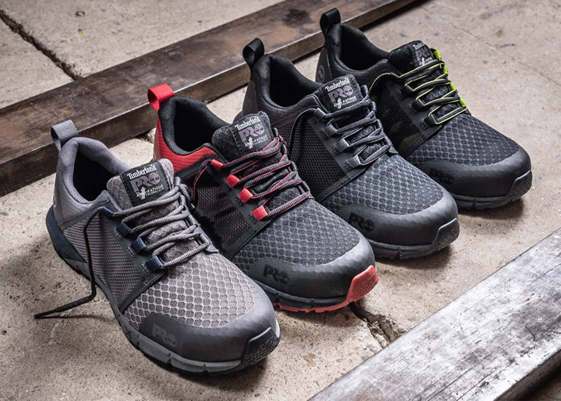 Four black work shoes lined up together on concrete with different bright pops of color at the laces and toe caps