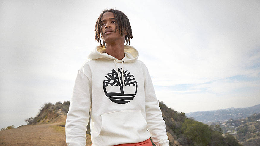 Image of a man in white Timberland hoodie with a black tree logo on the top of a hiking trail.