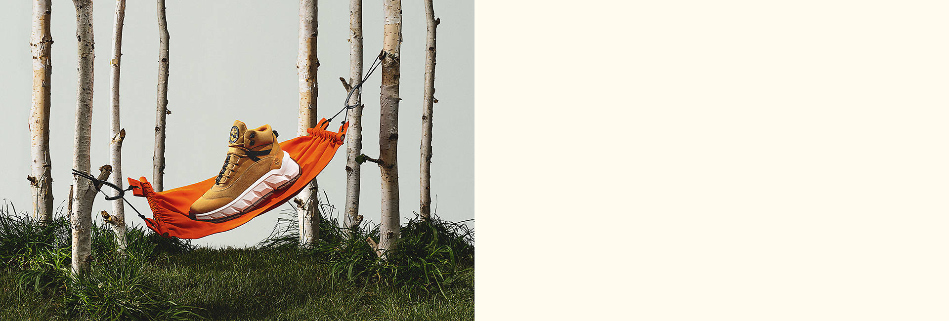 Image d'une botte basse fauve avec une épaisse semelle extérieure blanche, perchée sur un mini hamac orange suspendu entre des branches de bouleau.