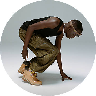 Crouched man wearing Timberland yellow boots, green pants and a black tank top