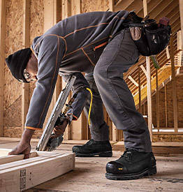 Image d'un homme portant des bottes de travail et une ceinture à outils travaillant à la charpente d'une maison.