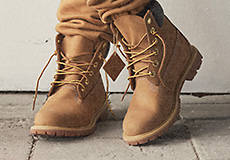 Close up image of a pair of wheat colored Timberland classic boots where the models left foot is crossing over their right leg.