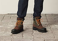 Image of a person in jeans from the middle of the shins to the ground, wearing Timberland boots and standing on paver stones.