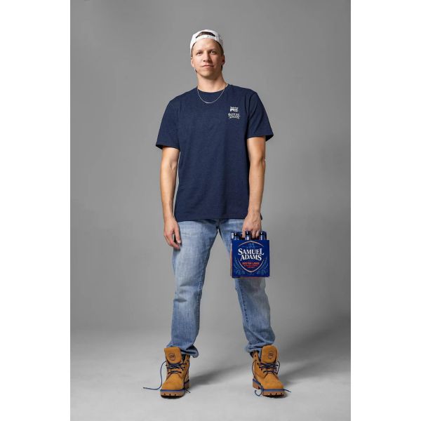 Man wearing Men's Sam Adams x Timberland PRO Beerproof T-Shirt and Men's Sam Adams x Timberland PRO Direct Attach Beerproof Boots while holding a Samuel Adam's Lager 6-Pack. Swipe right to get to the next product in the image carousel.