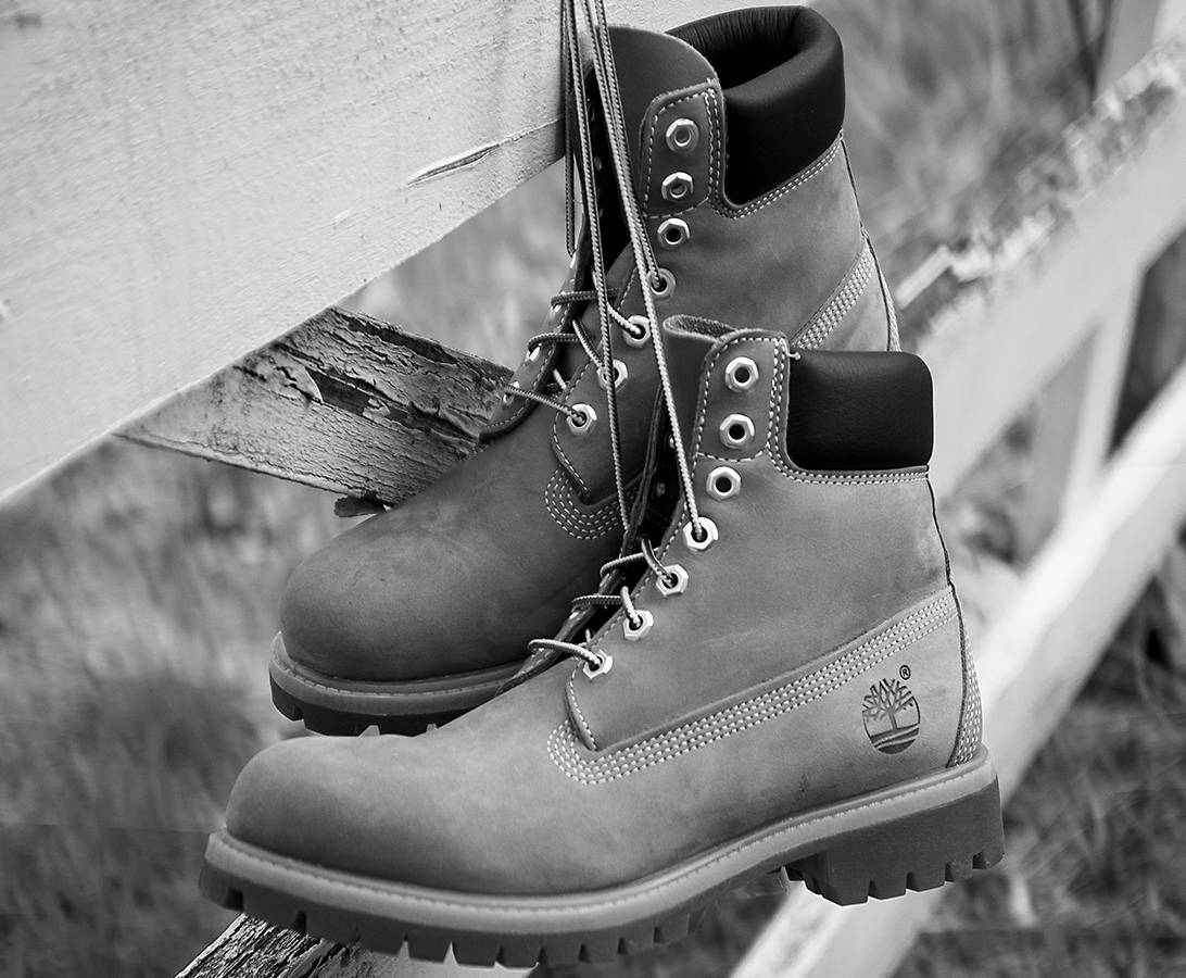 Black-and-white image of a pair of Timberland classic boots hanging by its laces against a white wooden fence.