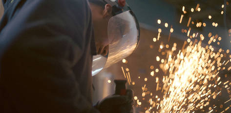 Image of Ralph as he is welding, wearing a welding mask as bright sparks shoot up into the air.